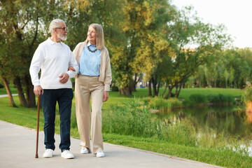 Obraz premium Lovely senior couple walking together near lake in park, space for text