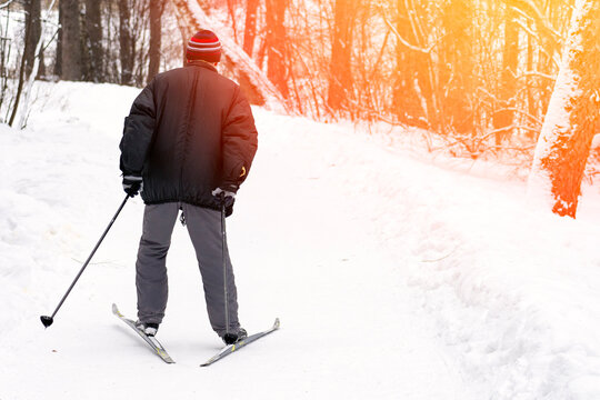 A man in a black jacket and gray pants is skiing on a snowy path. He is wearing a red hat and gloves