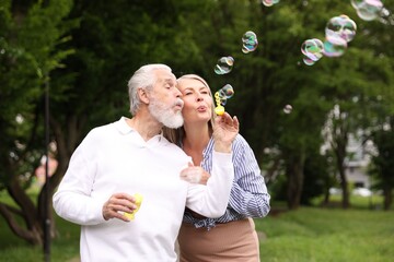 Lovely senior couple having fun with soap bubbles in park, space for text