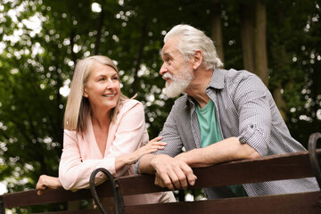 Lovely senior couple near wooden bench in park, low angle view