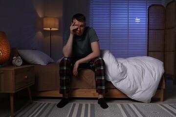Frustrated man suffering from insomnia on bed indoors