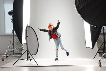 Little boy on light grey background in photo studio with professional equipment