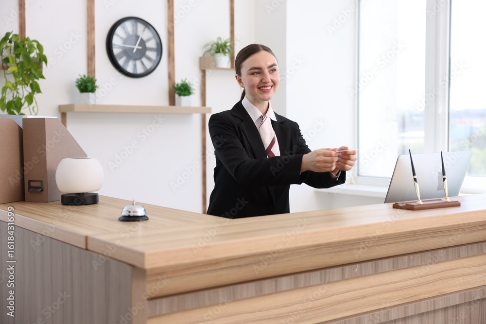 Poster smiling receptionist in uniform giving card key at reception desk in hotel