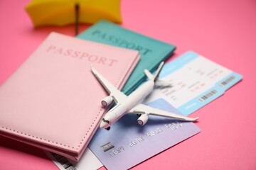 Airplane model, passports, flight tickets and credit card on pink background, closeup