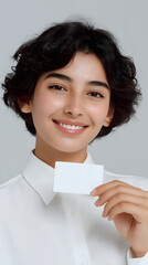 Young smiling woman with short curly hair holding small blank card in front of grey background, portrait for branding, identity mockup, business presentation, marketing, and promotional design