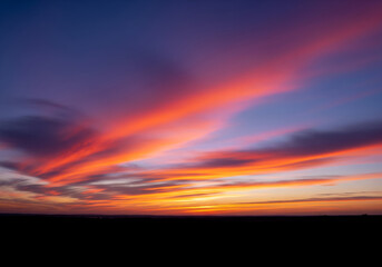 Obraz premium Dramatic sunset sky with vibrant orange and purple clouds over a dark horizon