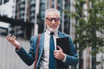 Real estate agency representative in a suit smiling outdoors holding a folder in an urban area near...