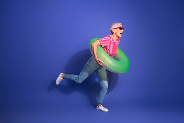 Cheerful senior woman in a striped shirt with a green float having fun against a vivid purple...