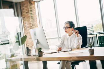 Confident businesswoman working in a modern office setting while reviewing documents at her desk...
