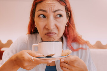 woman grimacing while sipping a cup of unpleasant coffee in a cafe, displaying clear signs of...