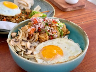 Chicken sambal matah rice bowl with mushrooms and sunny side up egg on a wooden table at a restaurant