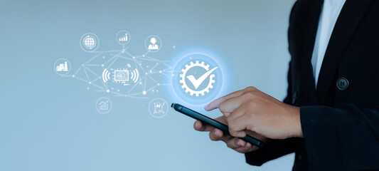 Close-up businessman hand using smartphone with holographic gear and check mark icon, digital automation, AI, and 5G network concept for business technology.