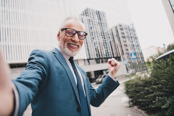 Smiling senior businessman celebrating success outdoors in urban setting wearing formal suit during...