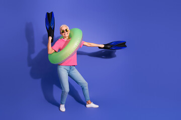 Joyful woman with short grey hair holding diving equipment and wearing summer outfit posing on...