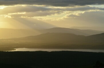 Sunbeams shine through a cloudy sky over Loch Morlich and Glenmore Forest Park in the Cairngorms National Park Scotland UK.