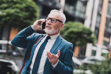 Confident elderly businessman negotiating on a phone call outdoors in urban city wearing a formal...
