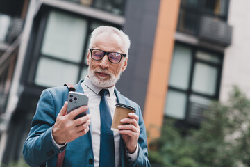 Professional senior businessman outdoors holding coffee and smartphone confidently looking at...