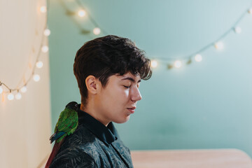A young woman with short hair closes her eyes as a green parrot perches on her shoulder. Soft...