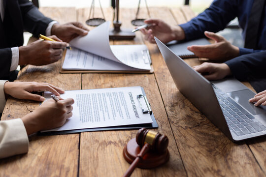 Lawyers and clients reviewing contract agreement terms before signing. Business partners carefully review contract terms before signing at a wooden table.