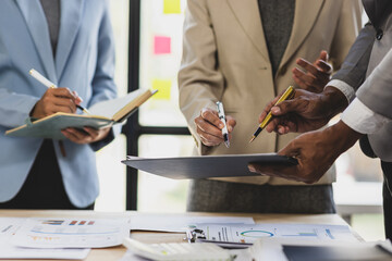 Business team is analyzing financial documents, pointing at charts and graphs, discussing strategies and collaborating on a project during a corporate meeting.
