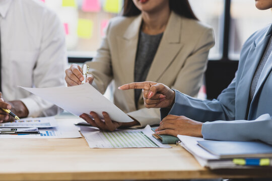 Business team is analyzing financial documents, pointing at charts and graphs, discussing strategies and collaborating on a project during a corporate meeting.