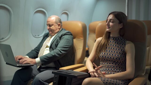 Western business class passengers, male and female, working or typing on a laptop while traveling on an airplane.