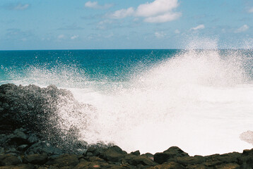 Ocean waves crash against rocky shoreline under a clear blue sky on a sunny day in a coastal location