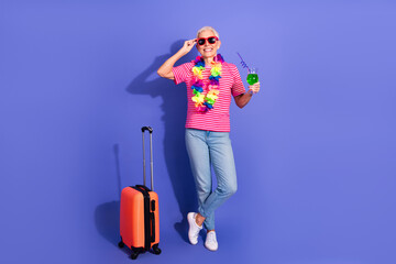 Cheerful Mature Woman Poses with Travel Luggage and Drink Against a Trendy Purple Background