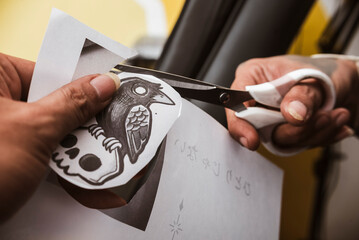 Tattoo artist finishes cutting a bird sitting on skull tattoo stencil from paper with scissors,...