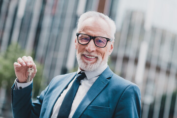 Senior businessman holding keys outdoors in urban setting, symbolizing real estate, property, and...