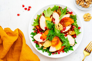 Yummy persimmon salad with grilled chicken, pomegranate, walnuts, oranges and lettuce, top view