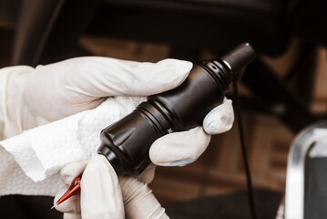 Close-up of gloved tattoo artist inserting a red needle cartridge into a black rotary tattoo pen...