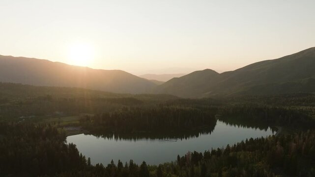 Aerial view of Payson lake surrounded by lush green forest, reflecting the warm glow of the setting sun behind the mountains, Payson, Utah, United States.