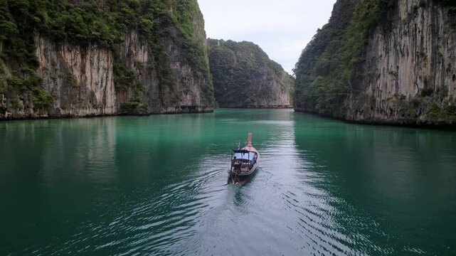 Aerial view of a boat sailing on the tranquil turquoise waters, surrounded by towering limestone cliffs covered in lush greenery, Pileh Leh Island, Tambon Ao Nang, Thailand.