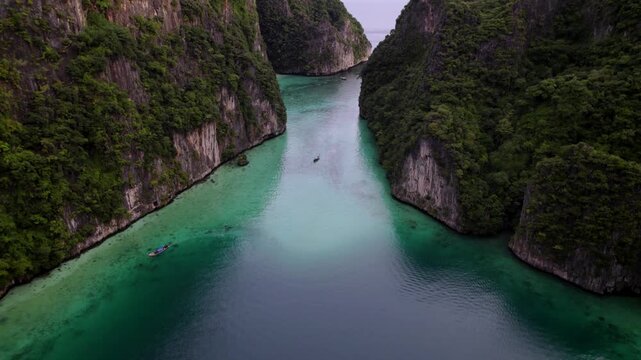 Aerial view of Pileh Leh Island, showcasing the lush green cliffs meeting the turquoise waters, with boats navigating the serene channel, Tambon Ao Nang, Thailand.