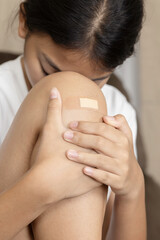 Sad girl holding her painful knee with a bandage after an accident. Childhood injury, hurt and pain concept. Unhappy child feeling ache from a scraped knee.