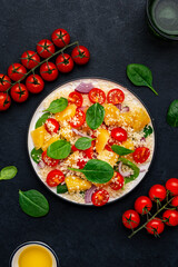 Gourmet vegan salad with couscous, tomatoes, onion, spinach and orange. Black background, top view