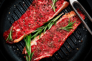 Raw beef sirloin steaks on grill pan, ready for cooking. Black background, top view