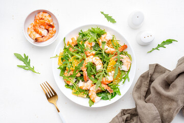 Delicious shrimp salad with juicy orange, fresh arugula and white sesame seeds on white plate, top...