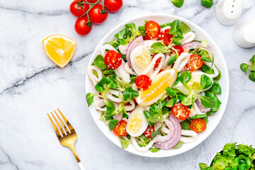 Gourmet seafood salad with squid, juicy orange, red tomatoes, lamb lettuce on marble table, top view