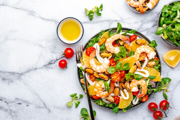 Delicious seafood salad with shrimp, mussels, squid, oranges, lettuce and lemon dressing, marble table, top view