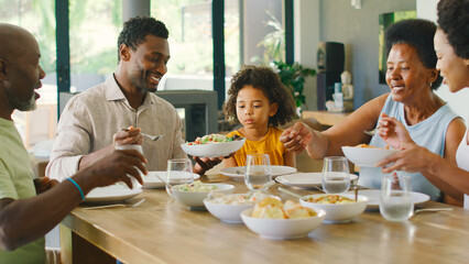 Multi-Generation Family Sitting Around Table Serving Food For Meal At Home
