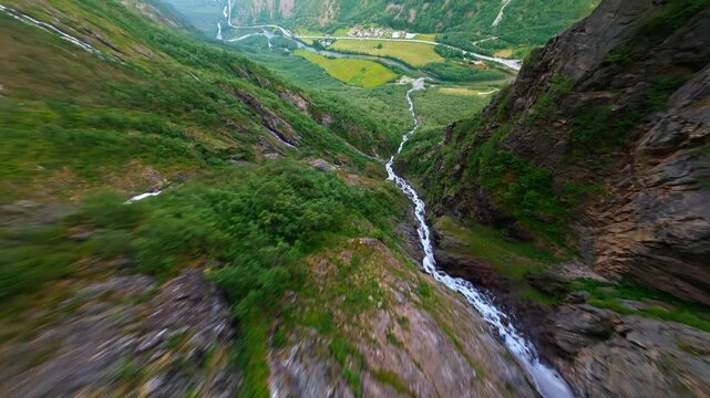 Aerial view of Geirangerfjord, a vibrant tapestry of lush green forests alongside a cascading river, nestled in the mountainous terrain, Stranda Municipality, Norway.