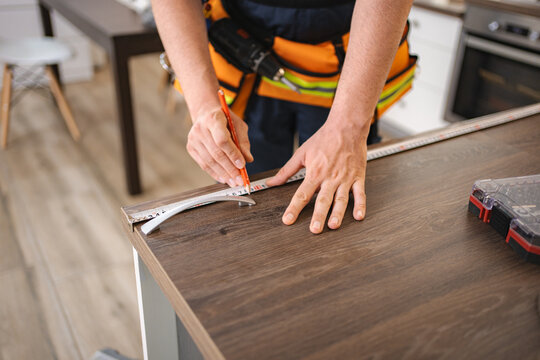 Carpenter measuring and marking wooden surface with pencil and ruler