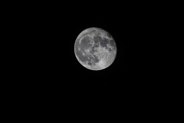 Big beautiful full round pale moon with craters in the night black sky	
