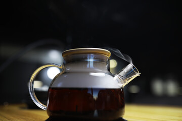 Steaming Glass Teapot with Freshly Brewed Tea on Wooden Table in Dim Lighting