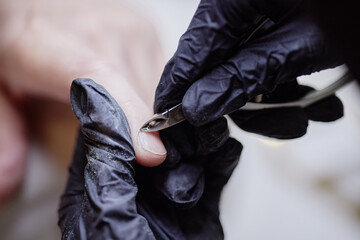 Caucasian adult hand receiving manicure from professional wearing black gloves, technician using...