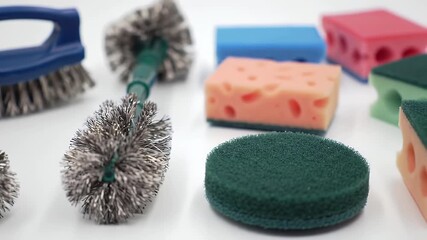 Diverse cleaning tools scrub brushes with metal bristles, and colorful sponges of varying textures and shapes, displayed on a white surface - Powered by Adobe