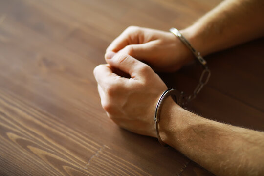 Close-Up of Hands in Handcuffs on Wooden Table - Arrest, Crime, Law Enforcement Concept