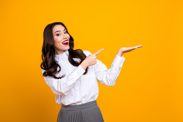 Smiling brunette woman in white shirt showing empty palm with finger gesture against vibrant yellow...